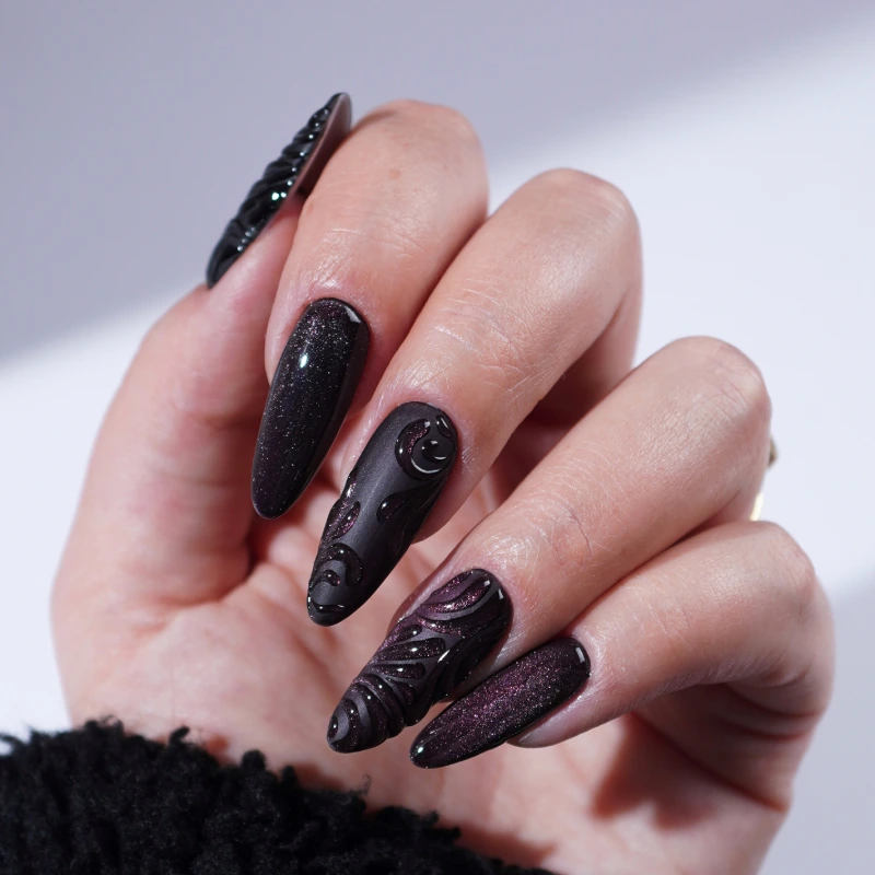 Dark nails in shades of black and plum with raised 3D embellishments.