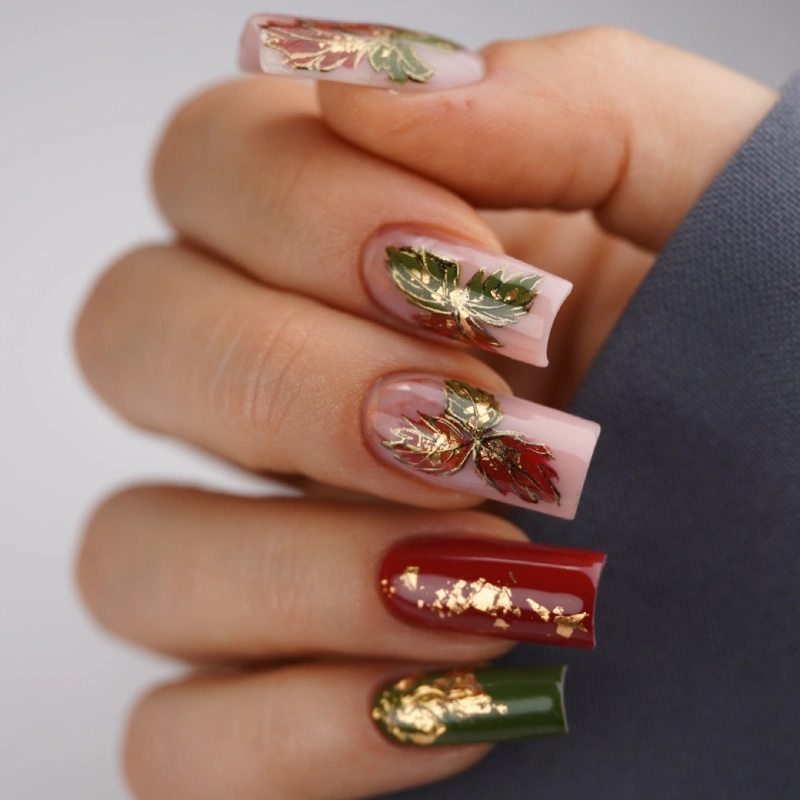 Ongles rouges avec feuilles dorées et touches vertes sur base nude
