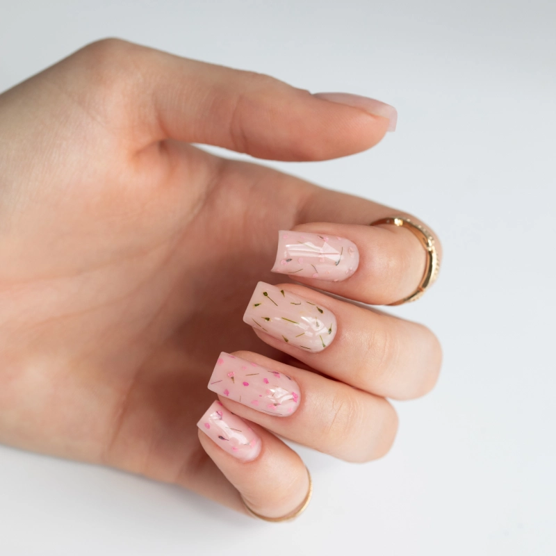 Jasnoróżowy manicure na kwadratowych paznokciach ozdobiony drobnymi suszonymi kwiatami